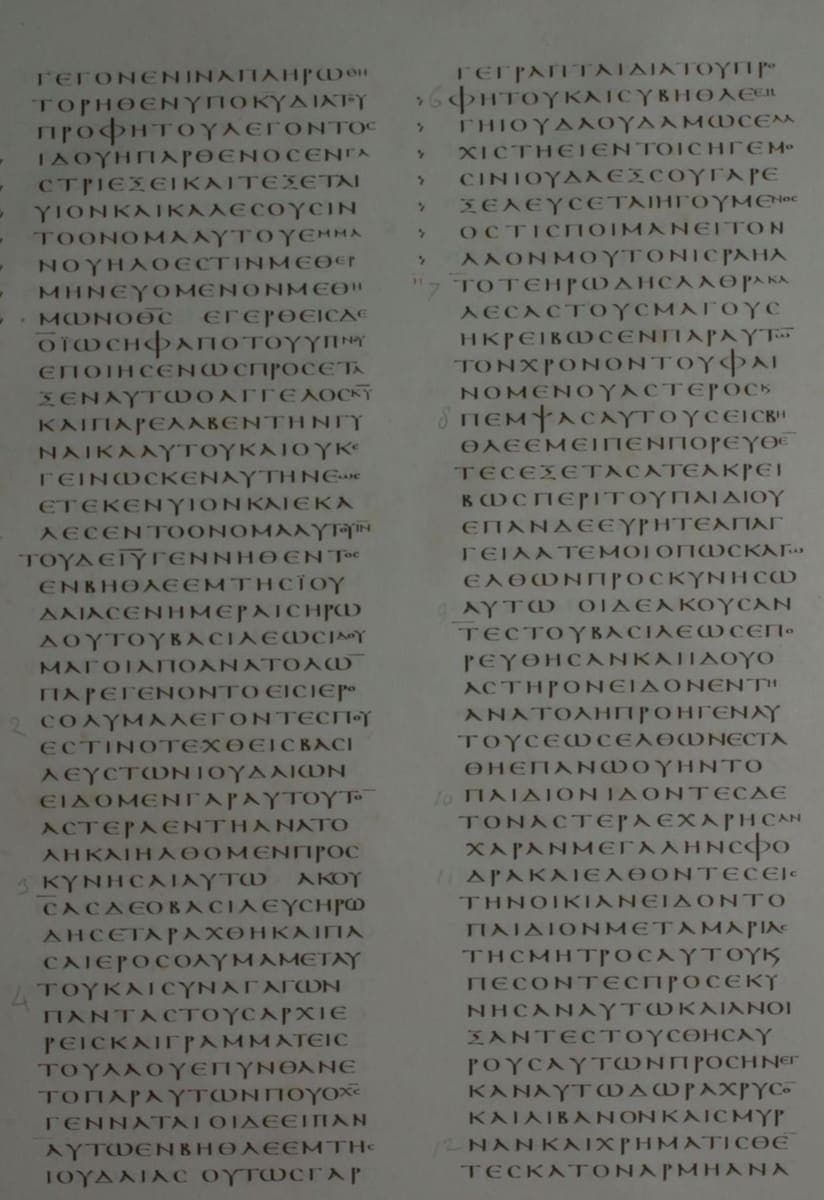 Two columns of small upright Greek capitals on grey-toned parchment, with printed numerals down the margins