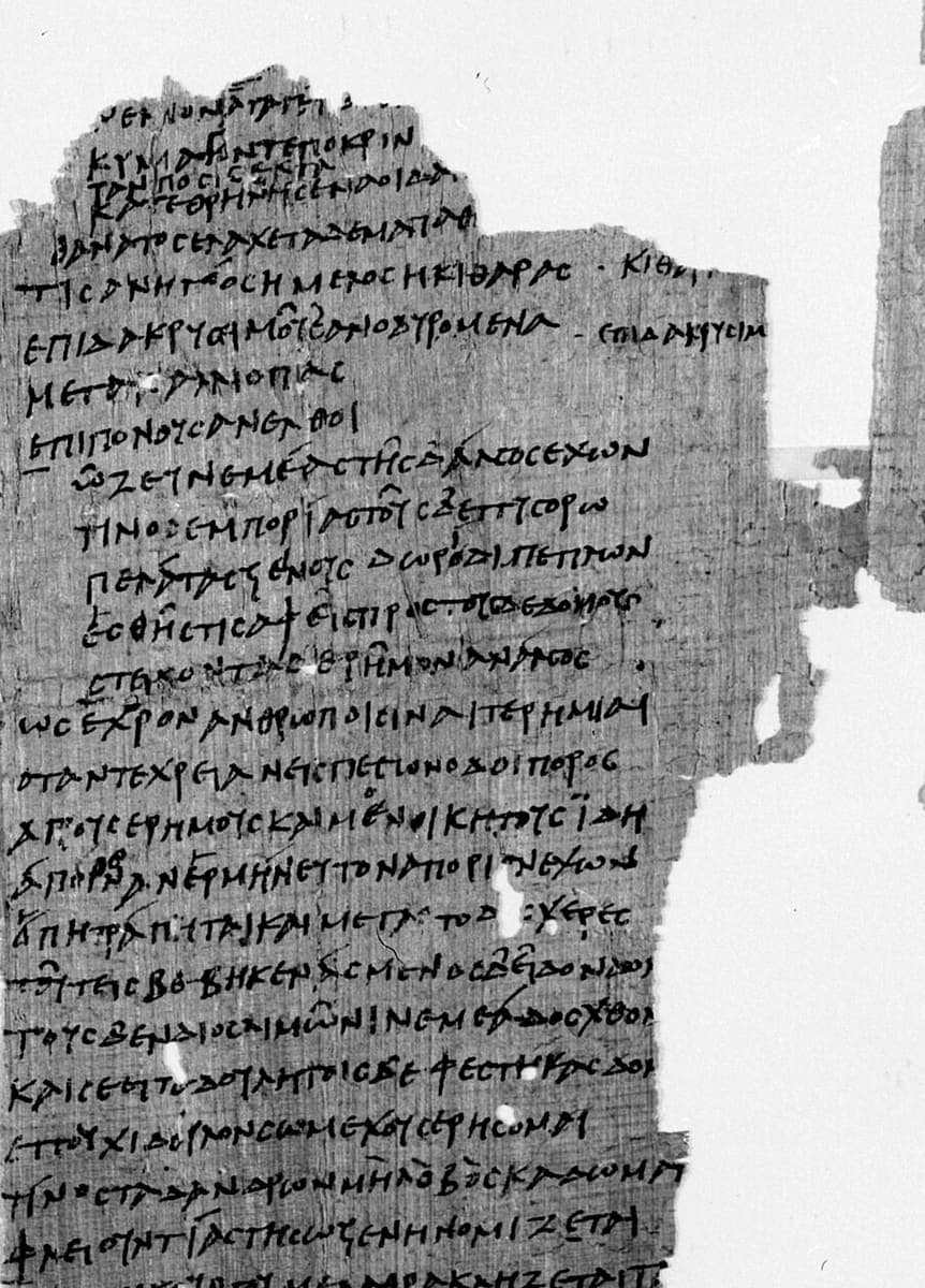Photograph of a ragged papyrus column carrying about thirty lines of rounded literary capitals, some lines set further to the left than others