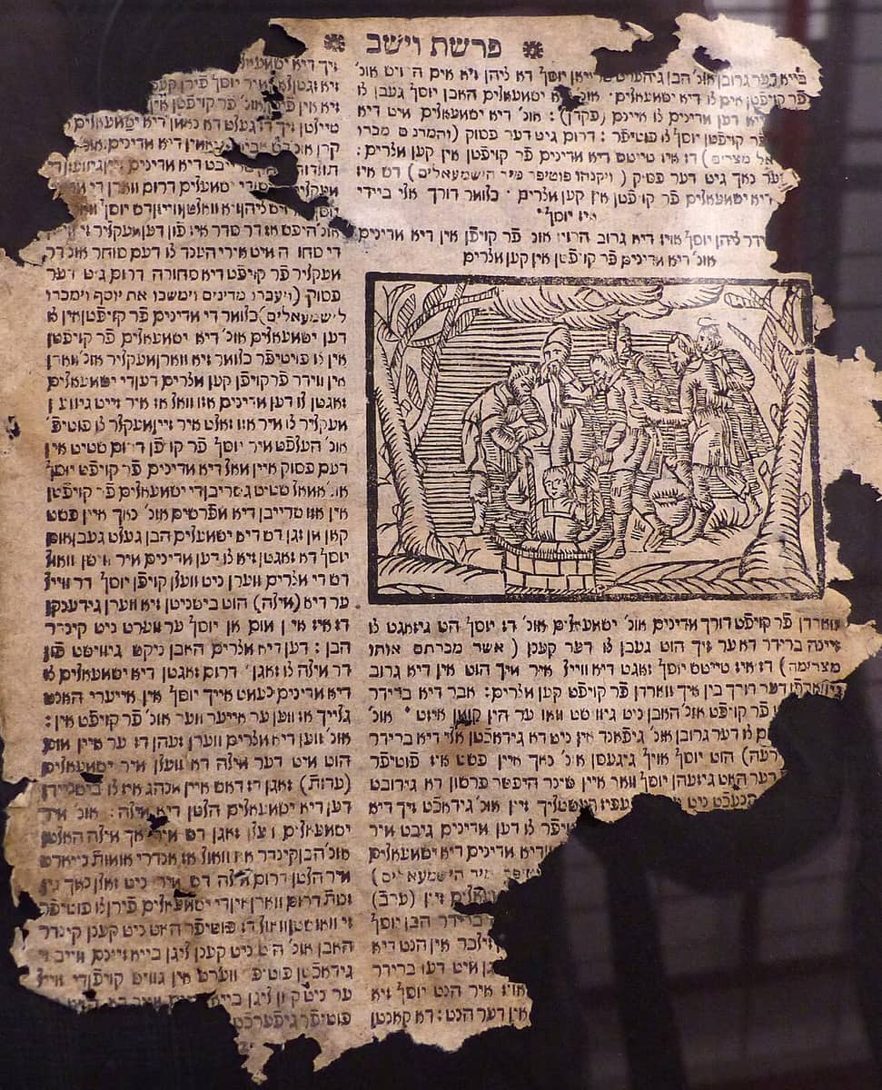 A torn and scorched printed leaf in Hebrew letters, two columns of text around a small woodcut of figures at a well