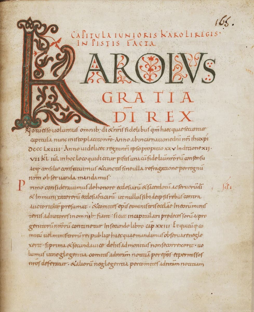 Decorated Carolingian minuscule page opening a royal capitulary, with a large initial K in “Karolus” and coloured display capitals