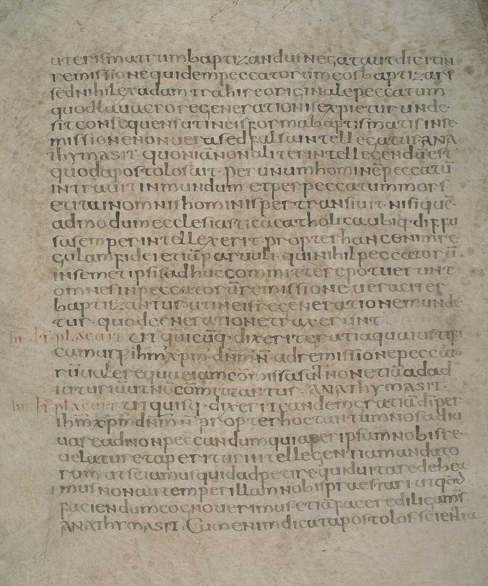 Full page of rounded sixth-century half-uncial canon law, with small red notes in the left margin where a new canon begins