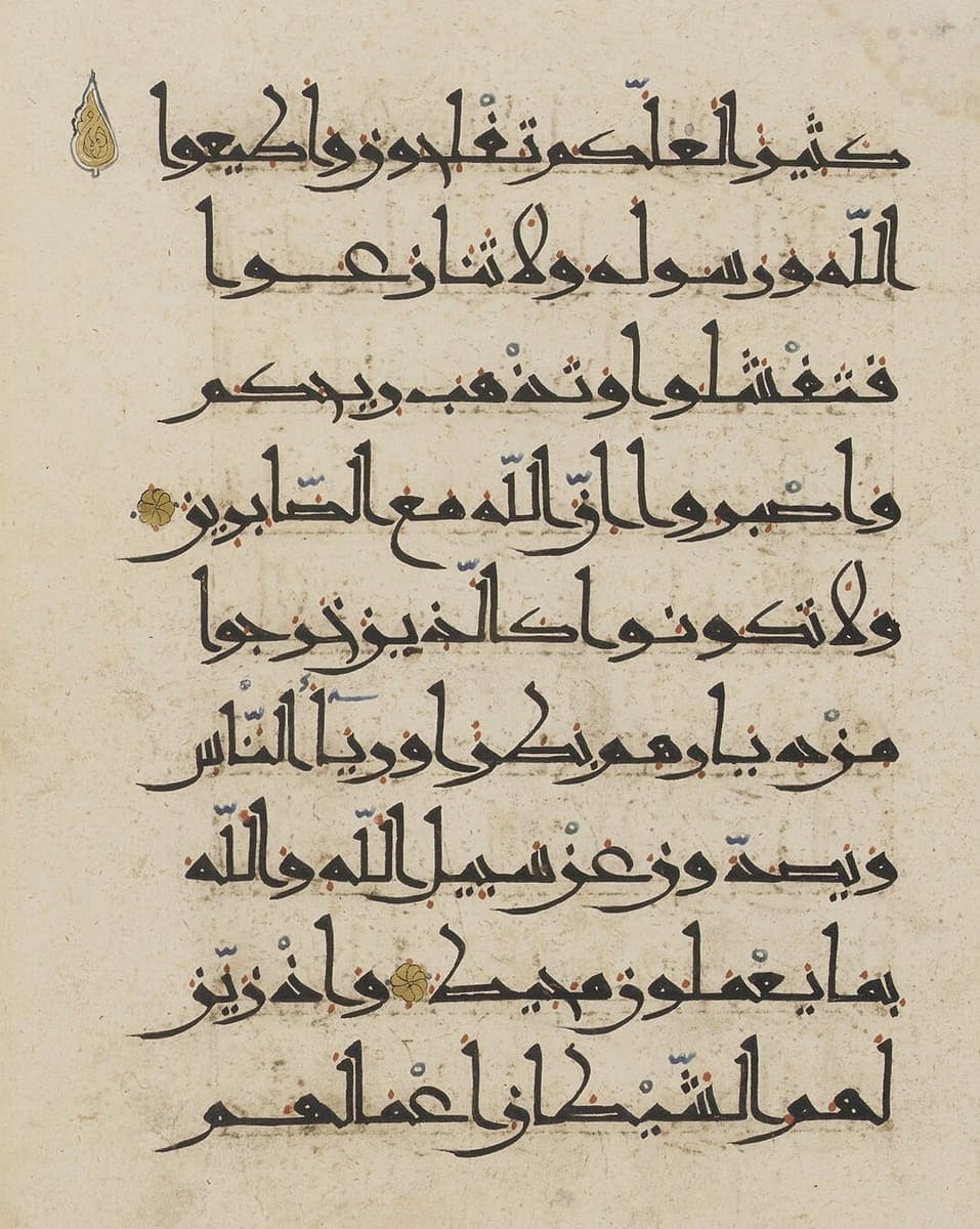 Nine lines of tall angular brown Kufic on cream paper with small red and blue vowel marks and two gold rosettes