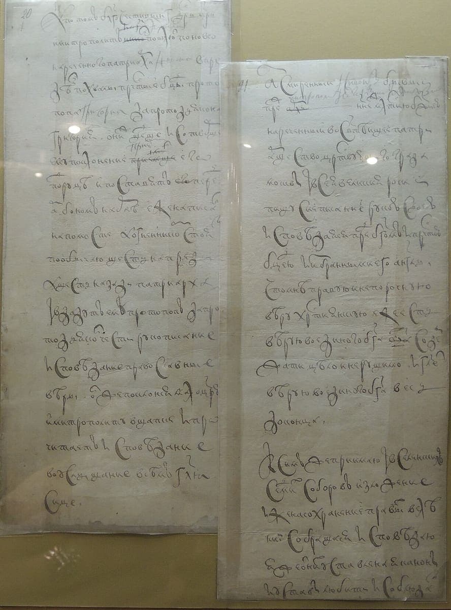 Two narrow strips of paper side by side under glass, each carrying short lines of seventeenth-century cursive with words struck through and small insertions above the line