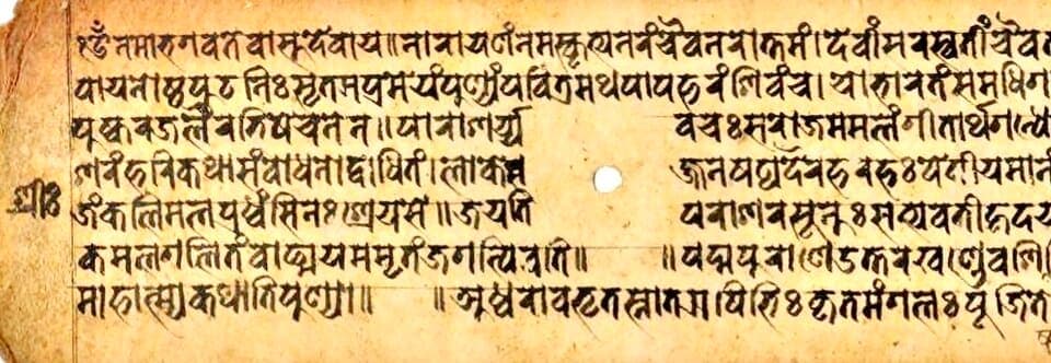 Yellow paper folio in landscape format with seven lines of Newar script, a small drawn circle standing in for the old binding hole and a numeral at the right edge