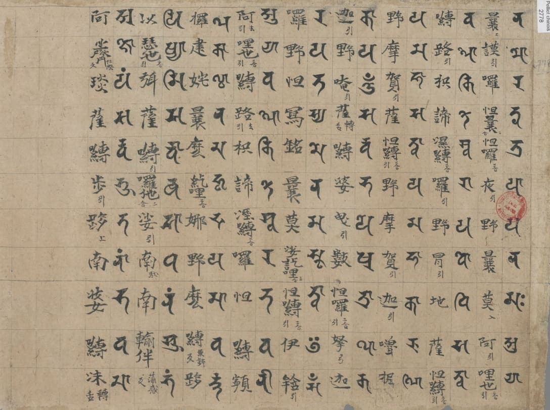 Ruled grid on brown paper with alternating columns of large Siddham syllables and Chinese characters, a red seal at the right edge