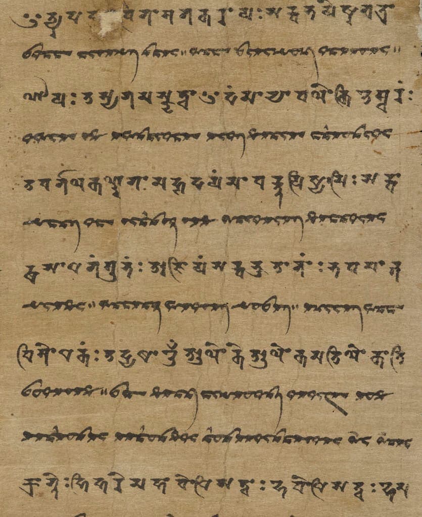 Strip of brown paper with alternating lines: large Siddham syllables above, dense cursive Sogdian script below