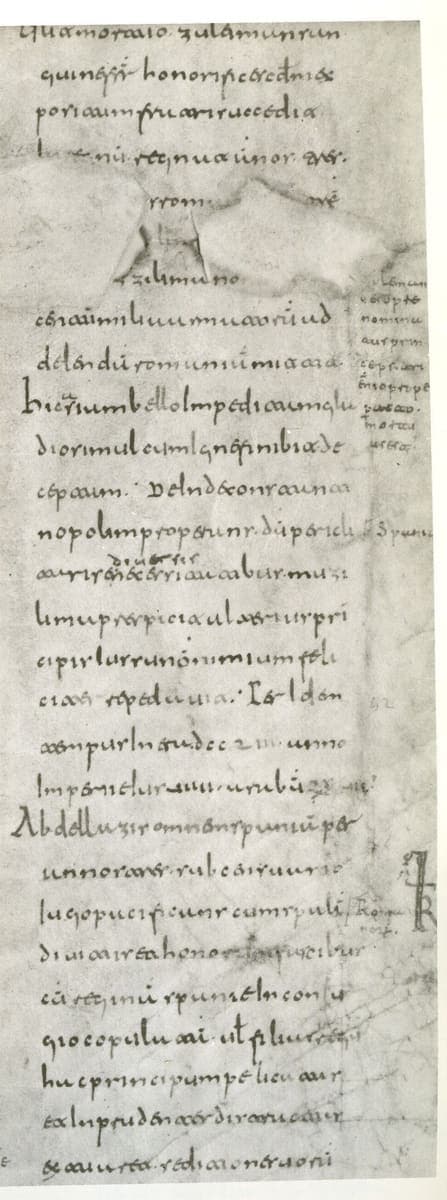 Black-and-white photograph of a narrow column of early Visigothic minuscule with a hole near the top and tiny marginal notes to the right.